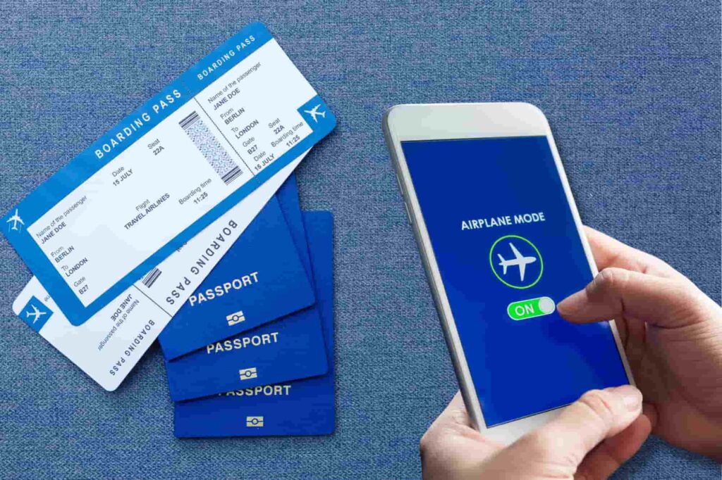 A person turning on Airplane Mode on a smartphone next to two boarding passes and a stack of passports.