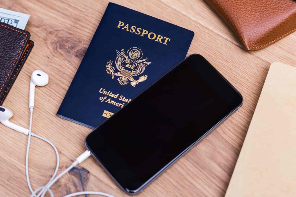 A United States passport, a black smartphone on a wooden desk.