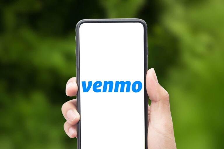 A hand holding a smartphone displaying the Venmo logo on the screen, representing Venmo’s public default privacy settings.