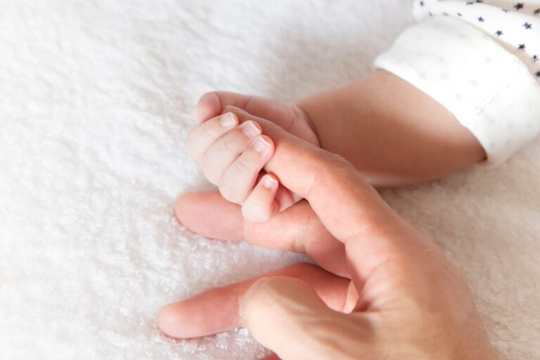A close-up shot shows a baby's hand grasping the index finger of a parent.