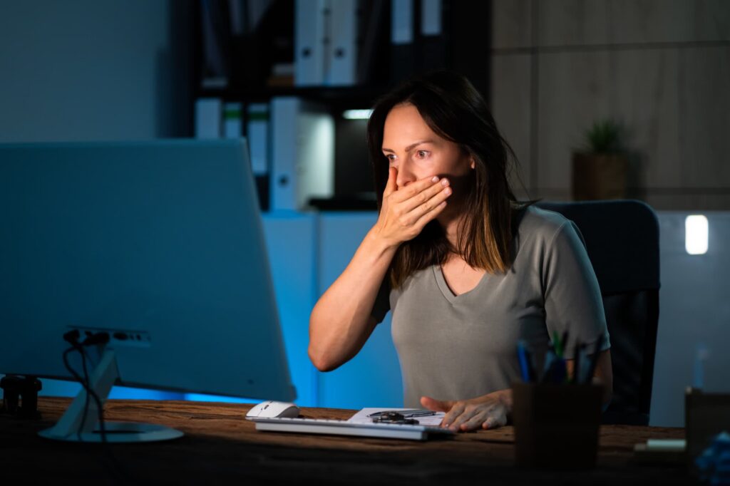 Person looking shocked while viewing a computer screen, illustrating the impact of a data breach, identity theft, or unauthorized access to personal information.