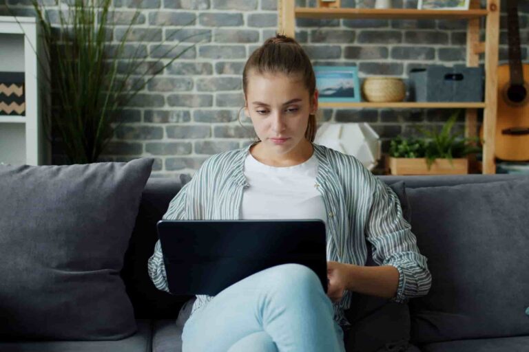 Young woman sitting on a sofa using a laptop in a home setting.